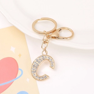Golden keychain with rhinestone-encrusted letter C pendant on a white ceramic plate