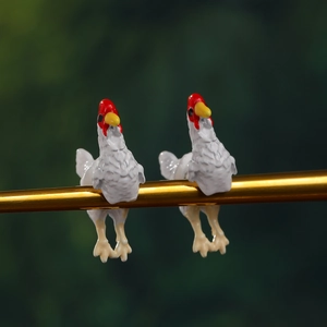 Dettaglio ravvicinato di orecchini a forma di gallo bianco con cresta rossa su barra