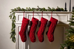 Set of four red cable knit Christmas stockings hanging on a white festive fireplace