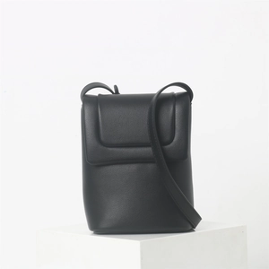Détail de la texture en cuir noir souple et du design minimaliste à rabat de ce sac bandoulière