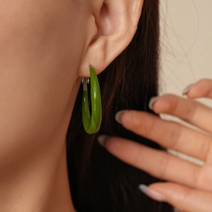 Primo piano di un orecchino a goccia verde minimalista con finitura lucida su una modella