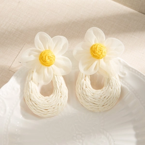 Detail of white mesh floral earrings with yellow stamen and woven straw pendants
