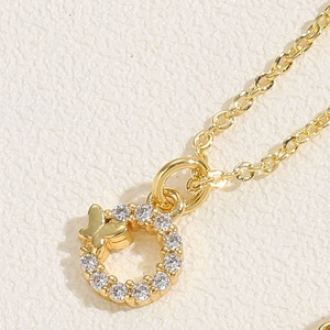Macro detail of a gold circle necklace featuring a zircon-studded butterfly pendant