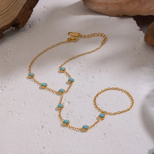 Detail of 18K gold plated finger chain bracelet featuring turquoise stones on stone surface