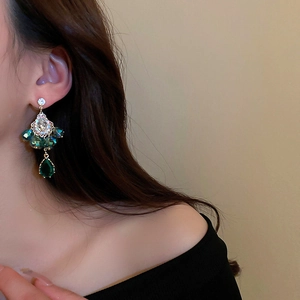 Close-up of bohemian water drop earrings with emerald crystals and gold metal setting