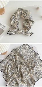 Detail of beige paisley silk scarf with blue patterns and a neat black border trim