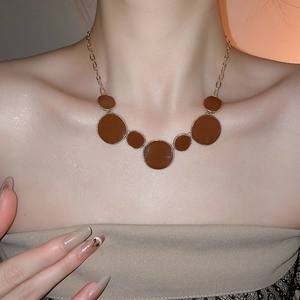 Détail d'un collier en chaîne dorée avec sept pendentifs ronds bruns sur un mannequin