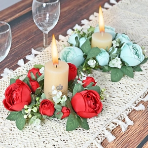 Close-up of artificial rose candle rings in red and mint green on a wooden table