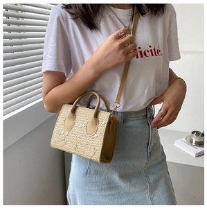 Detail of straw woven crossbody bag featuring floral embroidery and PU leather straps