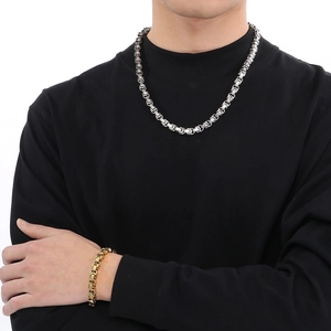 Détail du collier argenté et du bracelet doré avec maillons épais en acier sur un modèle