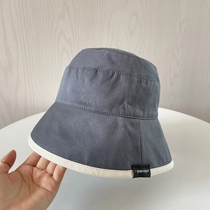Detail of grey canvas bucket hat featuring cream piping and a black brand label