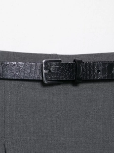 Detail of black faux crocodile leather belt with silver metal buckle on gray trousers