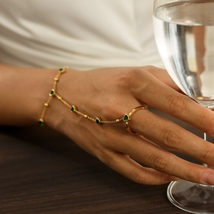 Detail of a gold finger bracelet with pear-cut green stones worn by a model