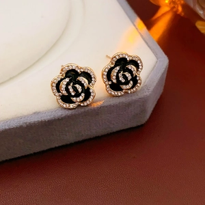 Close-up of black camellia stud earrings with gold edges and sparkling rhinestones