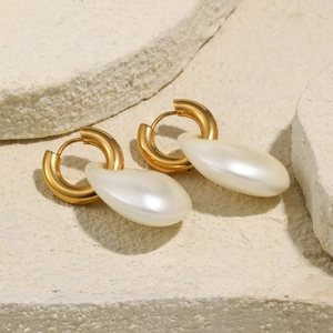Detail of gold hoops with large white teardrop pearls on a minimalist stone texture