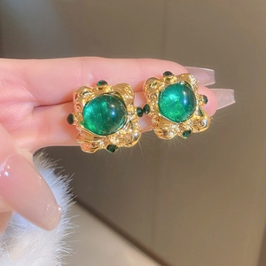 Close-up of vintage gold square earrings featuring emerald green gemstones in a retro style