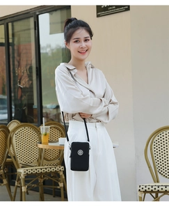 Sac bandoulière noir en nylon pour téléphone porté par un mannequin dans un café