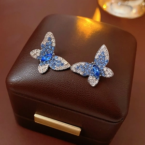 Primer plano de pendientes de mariposa con cristales azules y blancos sobre cuero