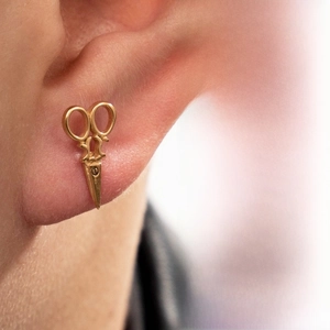 Détail d'une boucle d'oreille dorée en forme de ciseaux avec un design raffiné