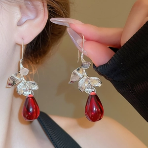 Detailed close-up of a silver leaf earring with a red teardrop pendant on model