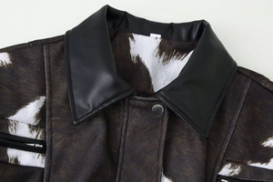 Detail of cow print jacket with black faux leather collar and metallic snap button
