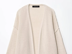 Dettaglio del cardigan in maglia grossa color panna con spalle scese e texture