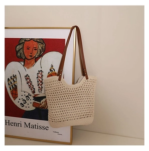 Detail of beige hollow woven tote bag with brown leather straps against artistic background