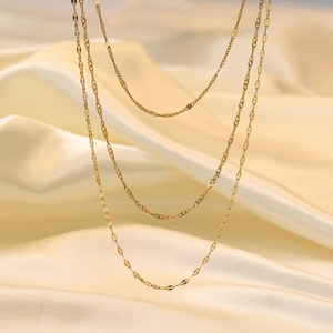 Close-up of triple-layered 18K gold plated titanium necklaces on beige silk background