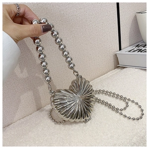 Detail of silver heart-shaped metal bag featuring radial texture and bead chain strap
