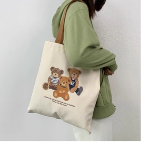 Detailed side view of a large cream canvas tote bag with cute bear prints on model