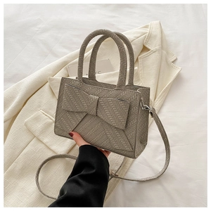 Detail showing the woven texture and large decorative bow on the grey crossbody handbag