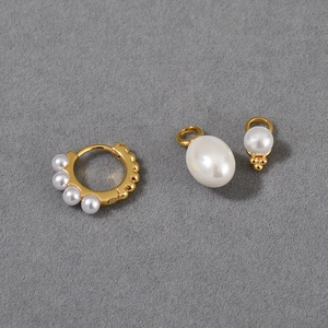 Detail view of detachable pearl pendants and gold hoop earring set on grey fabric