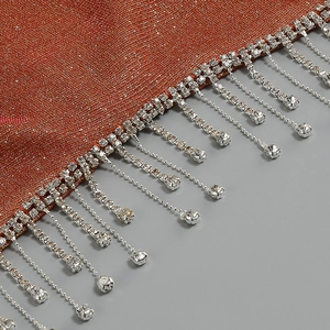 Dettaglio del crop top arancione glitterato con decorazione di frange in strass lucidi