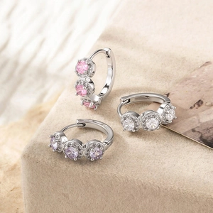 Three minimalist copper hoop earrings with pink purple white cubic zirconia on stone surface