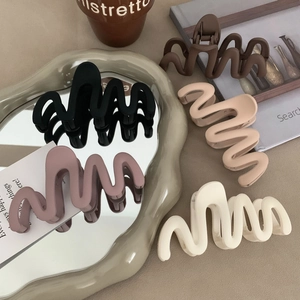 Five matte S-shaped wavy hair clips in earth tones displayed with lifestyle props
