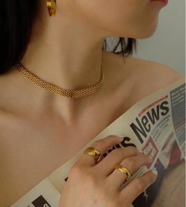 Primo piano della collana a maglia dorata e dell'anello con motivo a rombi su modella