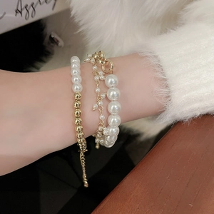 Detail of layered pearl bracelet set with gold OT buckle and charms on model wrist