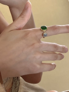 Detailed view of an open golden ring featuring square emerald green and grey gemstones