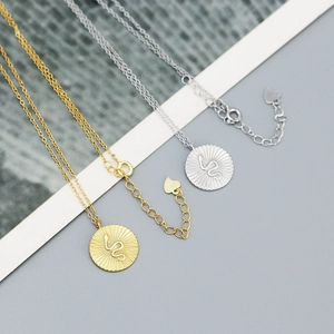 Detailed view of gold and silver snake round pendant necklaces on a minimalist background