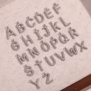 Full set of 26 silver twist-texture alphabet pendants arranged on beige fabric