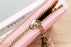 Detailed close-up of pink pebbled leather coin purse with gold zipper and fringe tassel