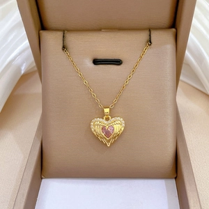 Macro view of golden heart necklace with pink stone and diamond wings in a jewelry box