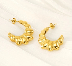 Detail of gold-plated C-shape croissant earrings with ribbed texture on soft fabric
