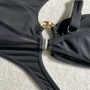 Detail of black swimsuit featuring golden metal ring connector and adjustable strap