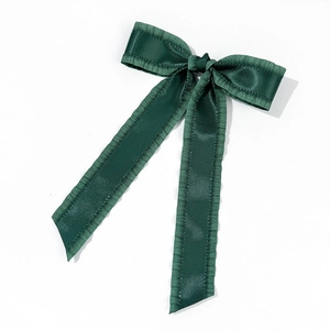 Detail of dark green satin bow hair clip with organza ruffle edges and long ribbons