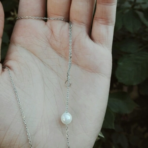 Detailed view of a silver minimalist pearl necklace held in hand with natural lighting
