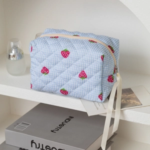 Détail de la trousse de maquillage matelassée avec motifs fraises et ruban en crème