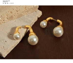 Dettaglio macro di orecchini vintage dorati con doppia perla su pietra ruvida