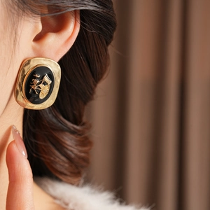 Close-up of vintage oval gold earrings with black enamel and a golden horse carriage relief
