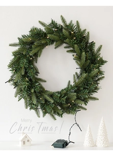 Detail of green PE Christmas wreath with warm LED lights hanging on a white wall
